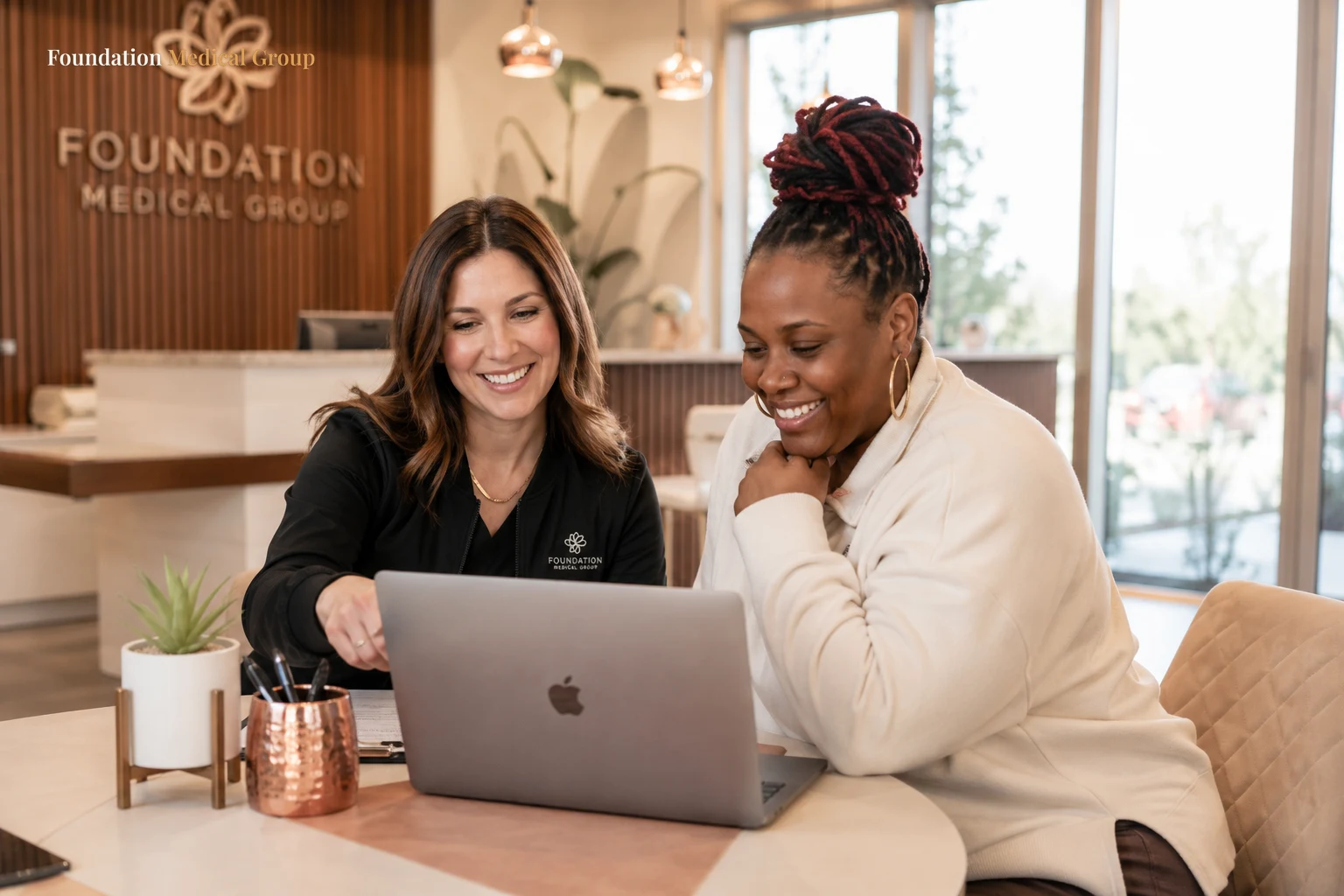 A friendly staff member and a relieved patient review coverage details together at a bright front-office desk with a lap