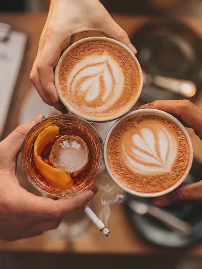 Two coffees and a cocktail glass on a table — the everyday choice between a morning and a night out that recovery is built around
